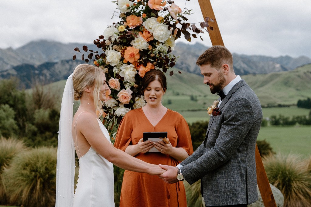 A couple standing under a wedding arch, with Poppy the celebrant officiating their wedding 