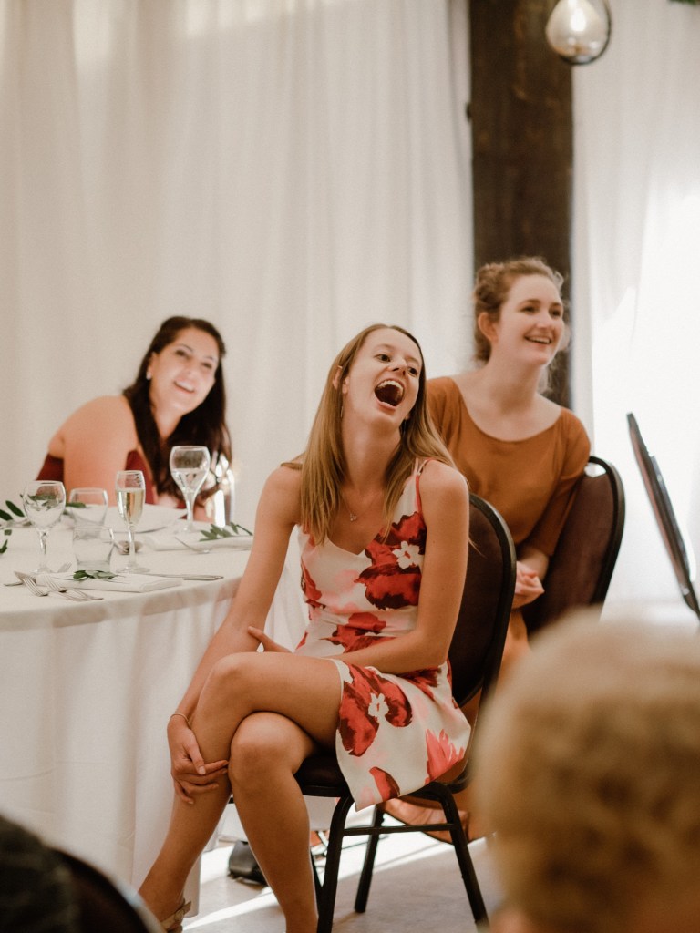 Wedding guests sitting at a table laughing at what a speaker (out of view) has to say