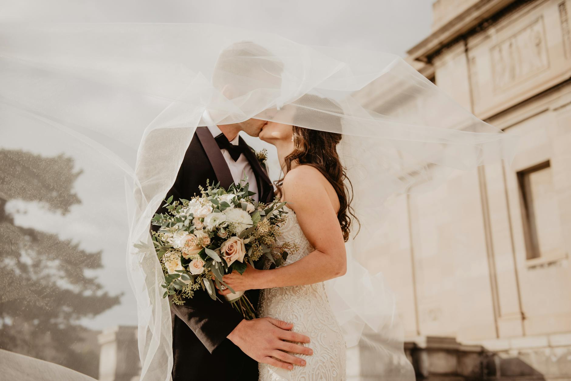 Bride and Groom kissing under her veil being blown in the wind